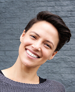 Woman with grey sweater smiling with head tilted