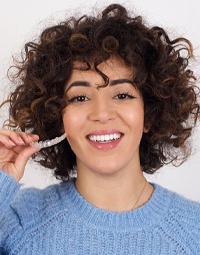 a person smiling and posing with an Invisalign tray in their hand