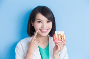 Smiling Burleson dentist holding model jaw with dental implant