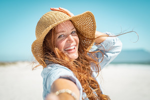 Woman on beach wearing straw hat and laughing