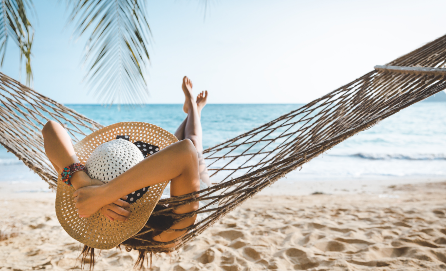 Woman on beach in hammock, face obscured by large hat